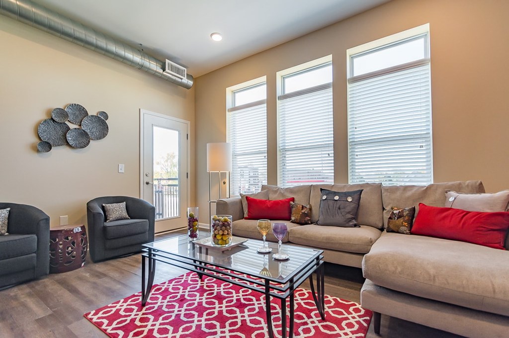 A living room with a glass coffee table and a couch with red pillows.