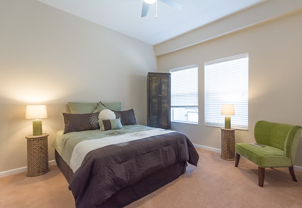 A bedroom with a bed, chair, and two lamps.