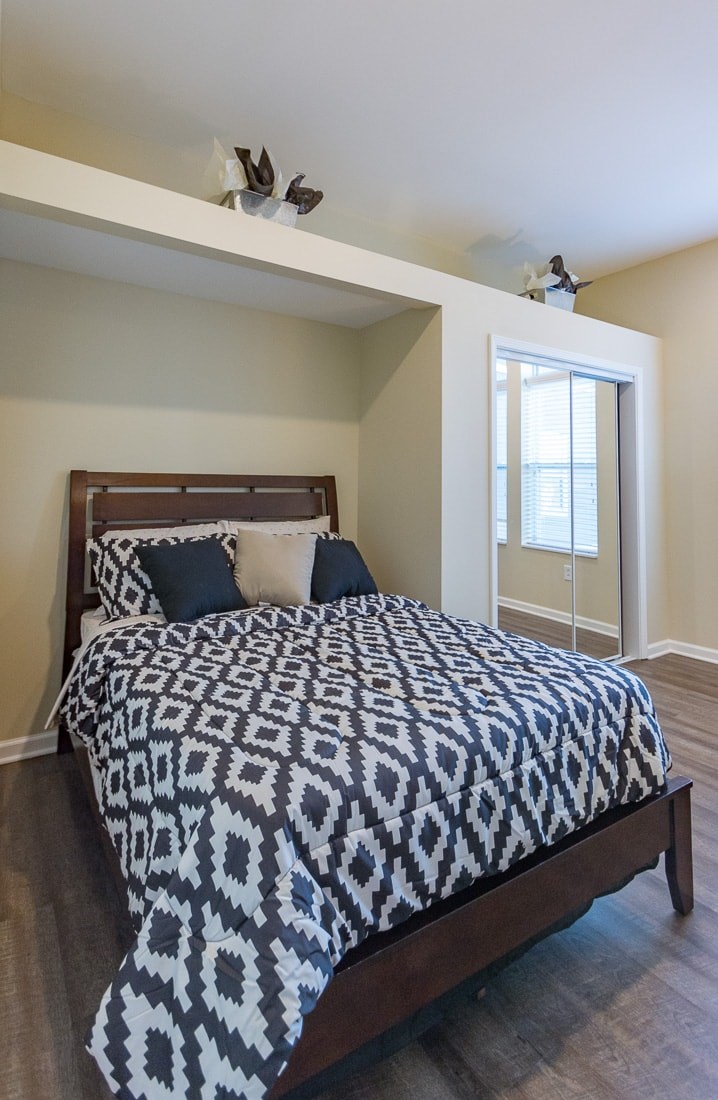 A bed with a black and white patterned comforter sits in a room with a window.