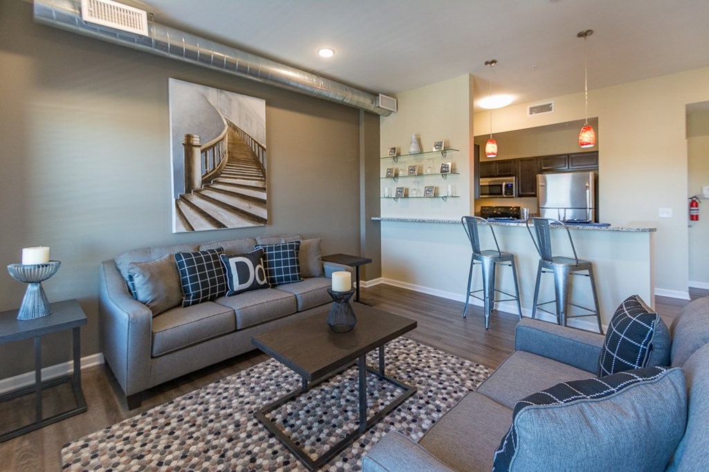 A living room with a grey couch and a painting of a staircase on the wall.