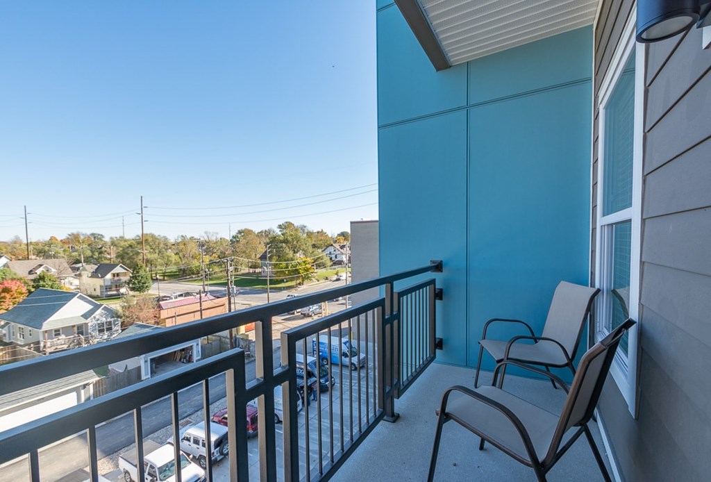 A balcony with two chairs and a railing overlooking a parking lot.