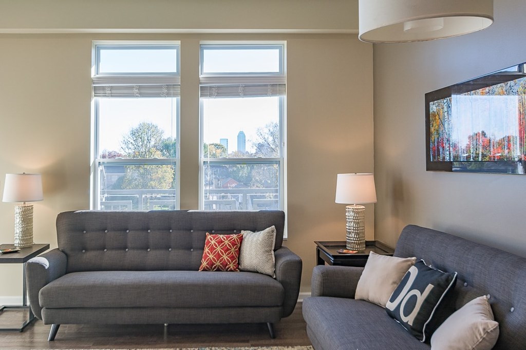 A grey couch with a red pillow and a black pillow with white letters on it.