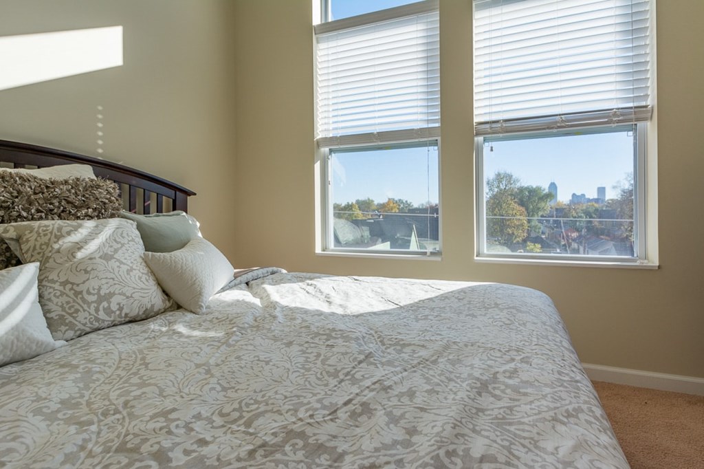 A bedroom with a large bed and a window overlooking a cityscape.
