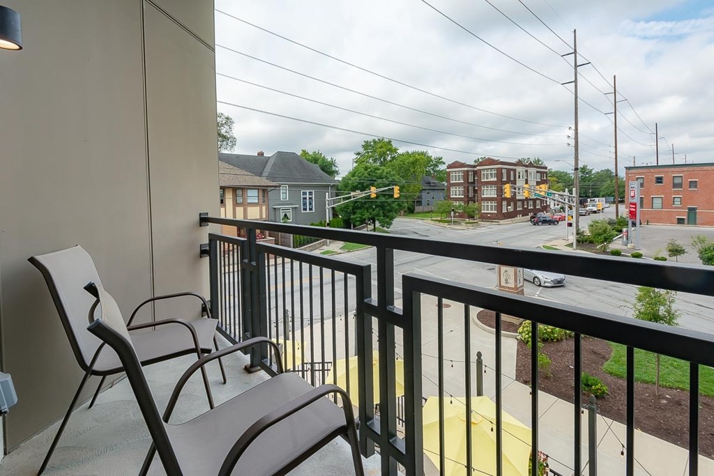 Two chairs are on a balcony overlooking a street.