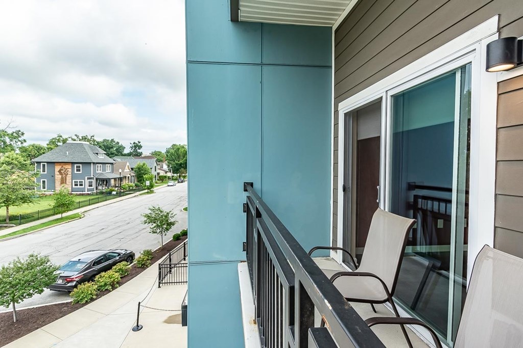 A balcony with a chair and a table overlooking a street.