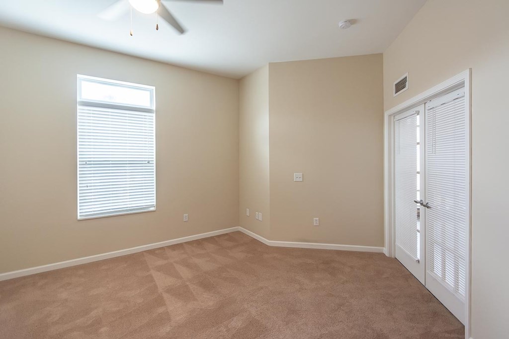 A room with a carpeted floor, a window with blinds, and a ceiling fan.