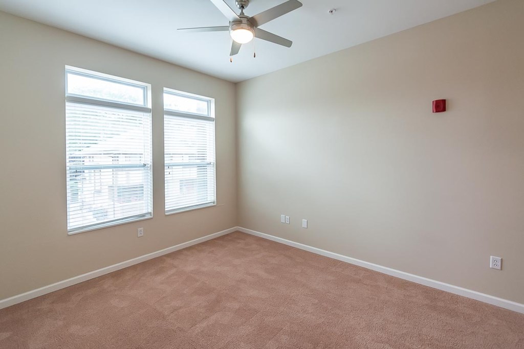 A room with a ceiling fan and two windows.