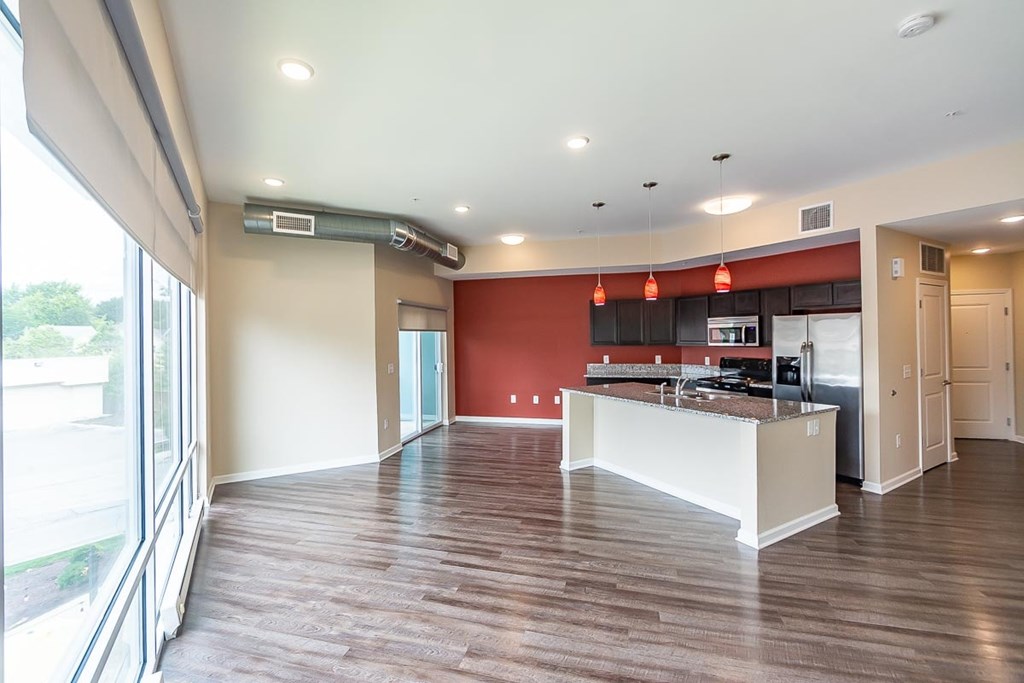 A kitchen with a red wall and wooden floors.