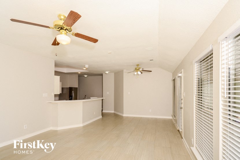 an empty living room with a ceiling fan and a kitchen