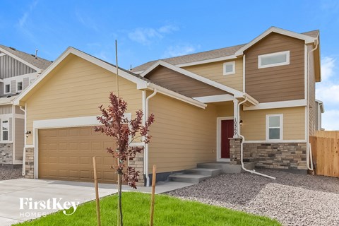 a beige house with a garage and a tree in the driveway