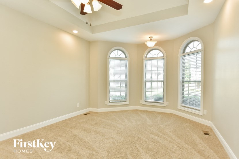 an empty living room with three windows and a ceiling fan