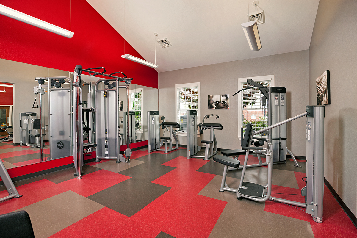 a gym with cardio equipment and a red floor