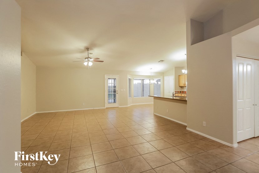 an empty living room with a kitchen and a ceiling fan