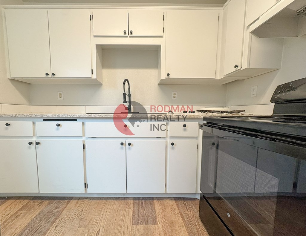 A kitchen with white cabinets and a wooden floor.