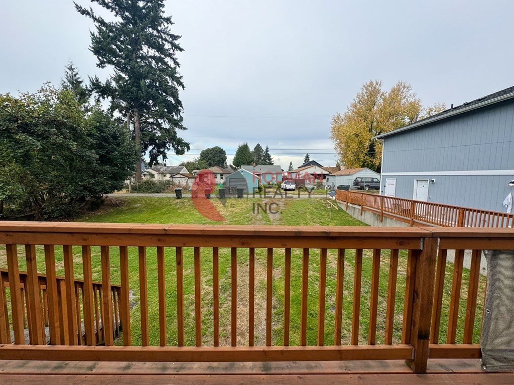 A wooden deck overlooks a yard with a red house and a tree.