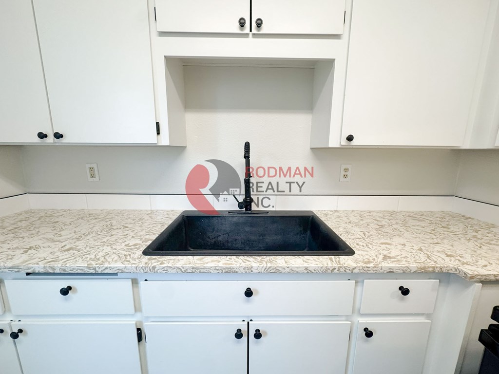 A kitchen with white cabinets and a sink in the middle.