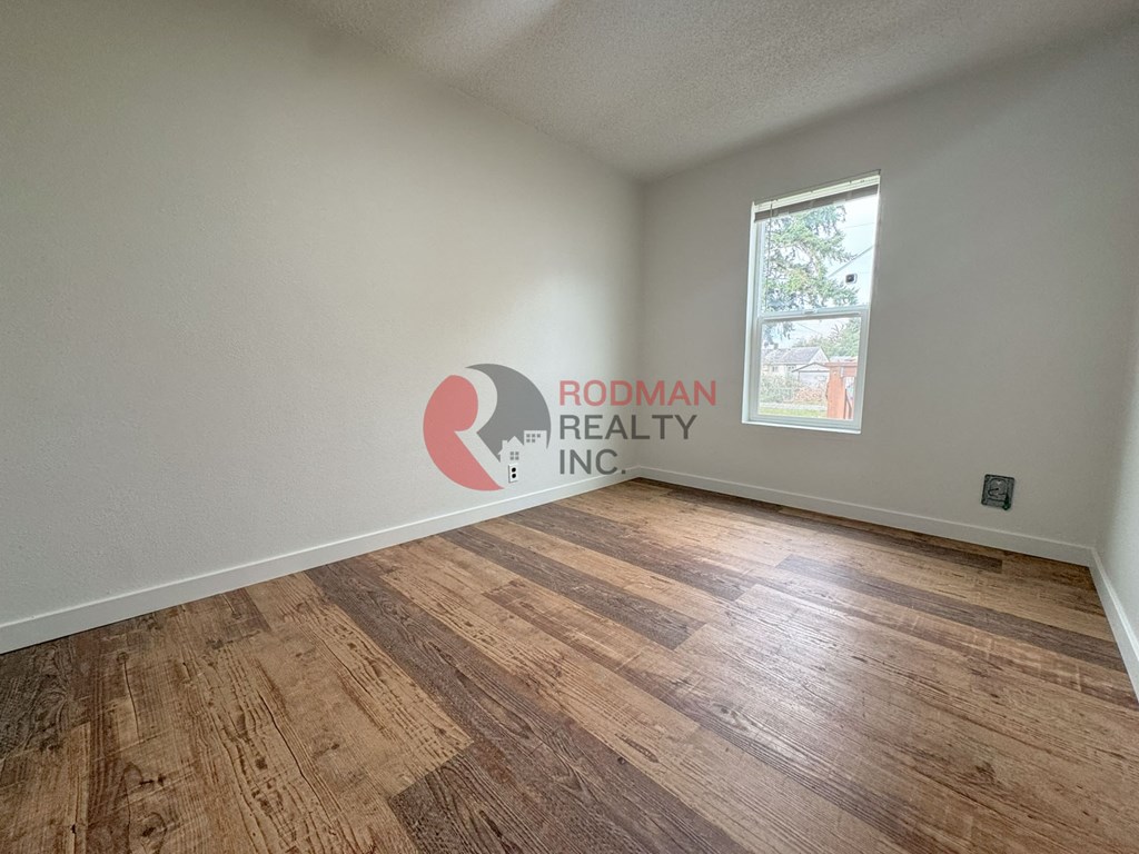A room with wooden flooring and a window, branded with Rodman Realty.