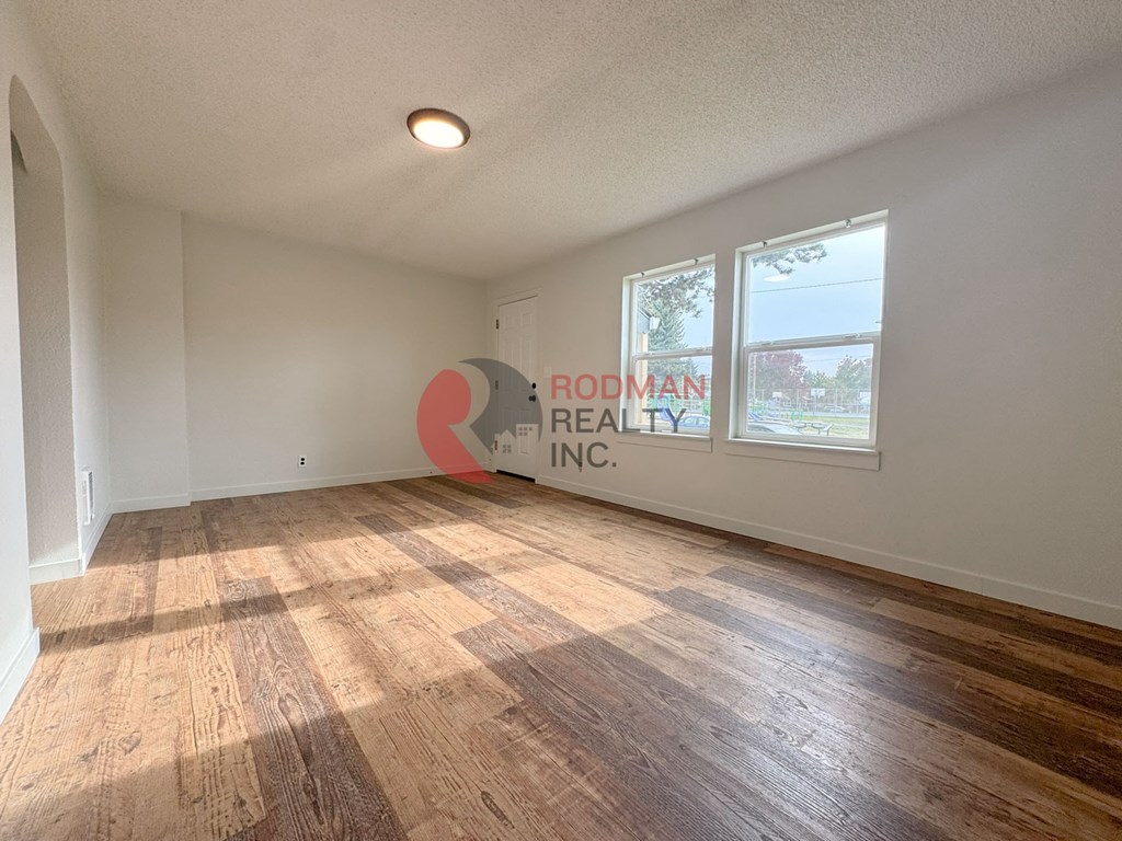 A room with wooden flooring and a window showing a view of a tree and a building outside.