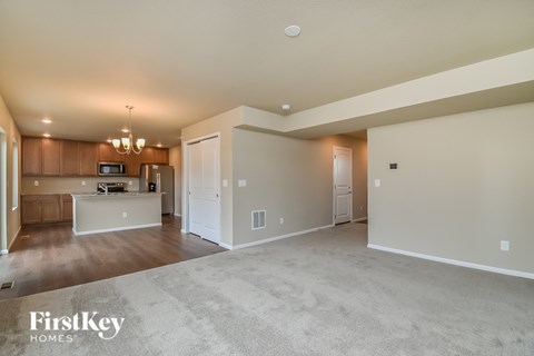 A spacious living room with a kitchen in the background and a carpeted floor.
