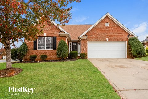 A brick house with a garage door and a tree in front.