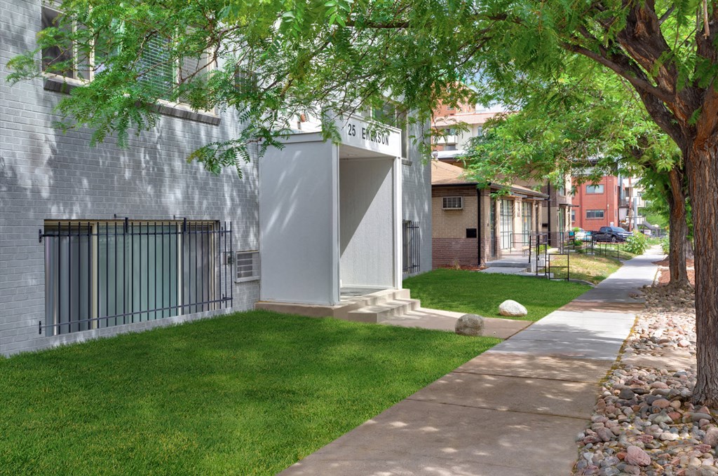 a sidewalk in front of a building with grass and trees
