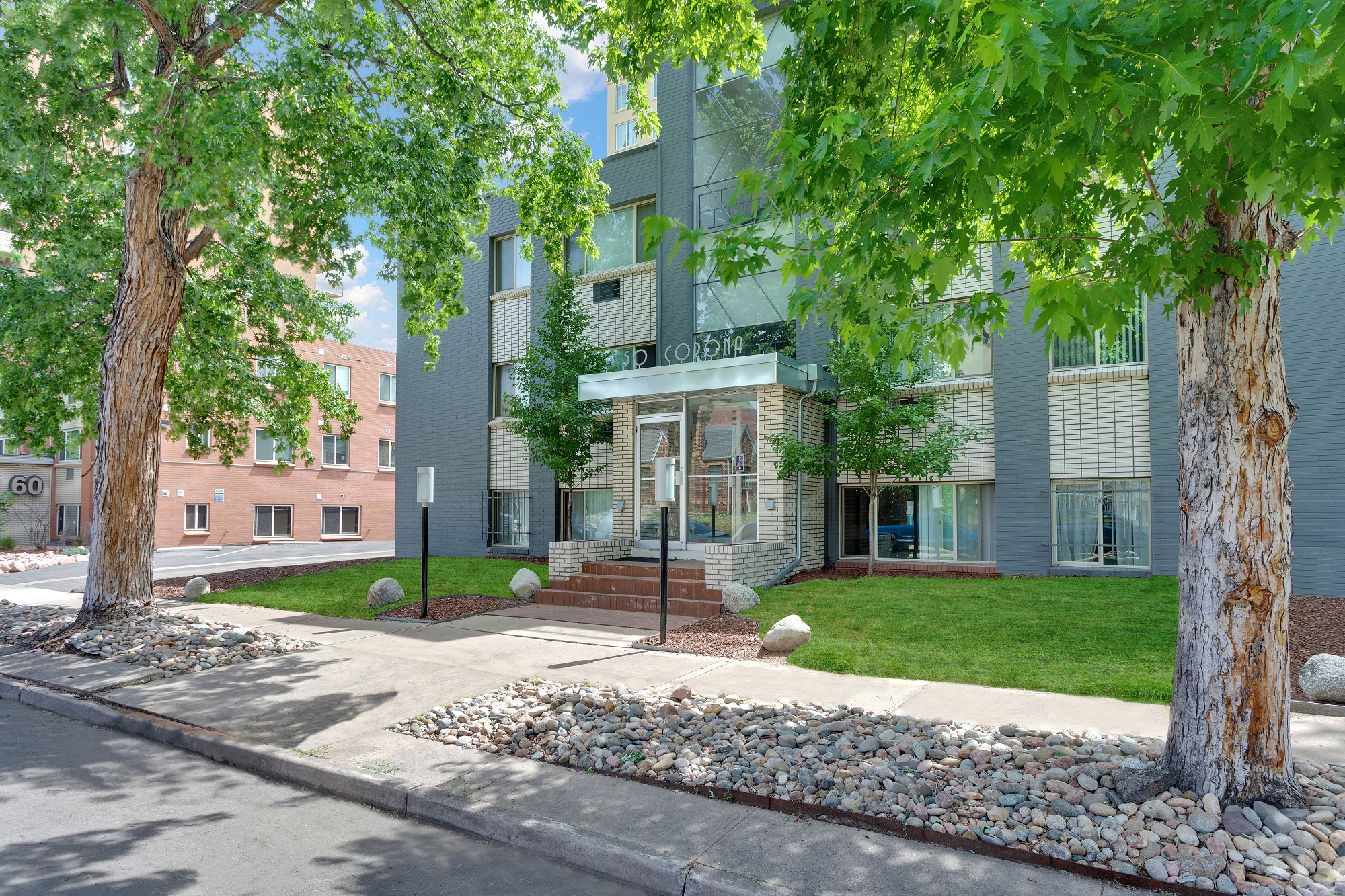 front view of an apartment building with trees and a sidewalk
