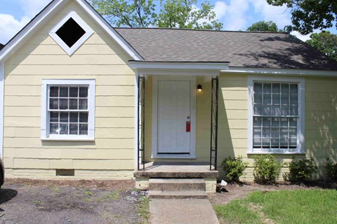 A small yellow house with a white door and windows.