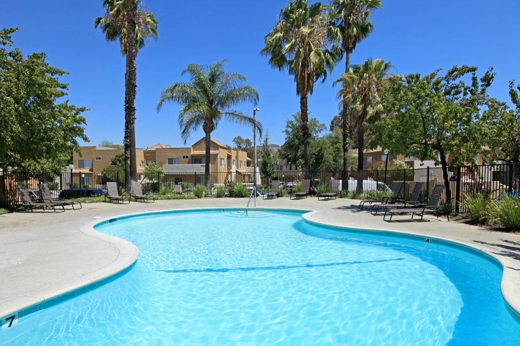 a large swimming pool with palm trees and buildings in the background