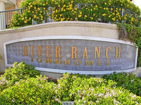A sign that says River Ranch Townhomes is surrounded by greenery.