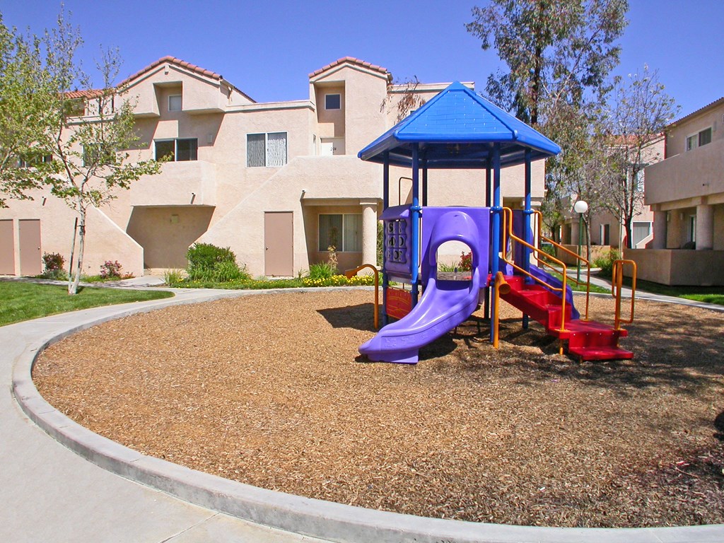a playground with a blue and red swing set in front of an apartment building