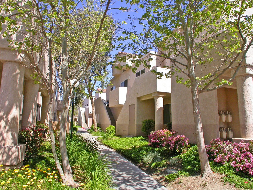 the walkway to the apartments is lined with trees and flowers