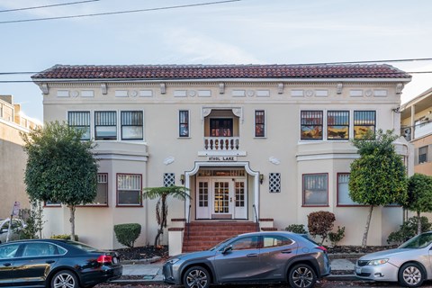 A white two-story building with a red tile roof and a sign that reads "ST. LAKES" sits on a street with cars parked in front.