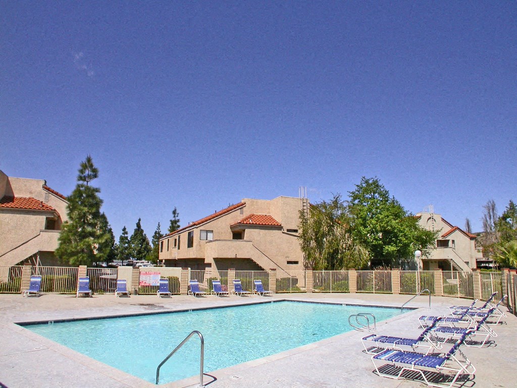 an outdoor pool with chairs and a building in the background