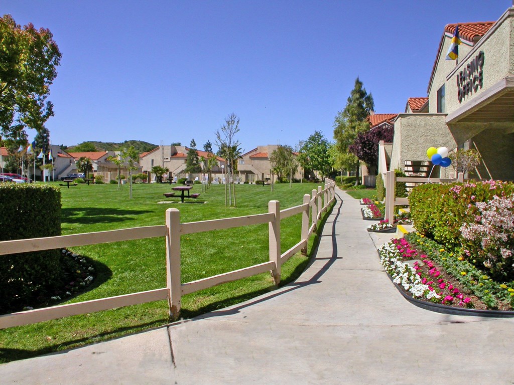 a sidewalk in front of a house with a yard and a fence
