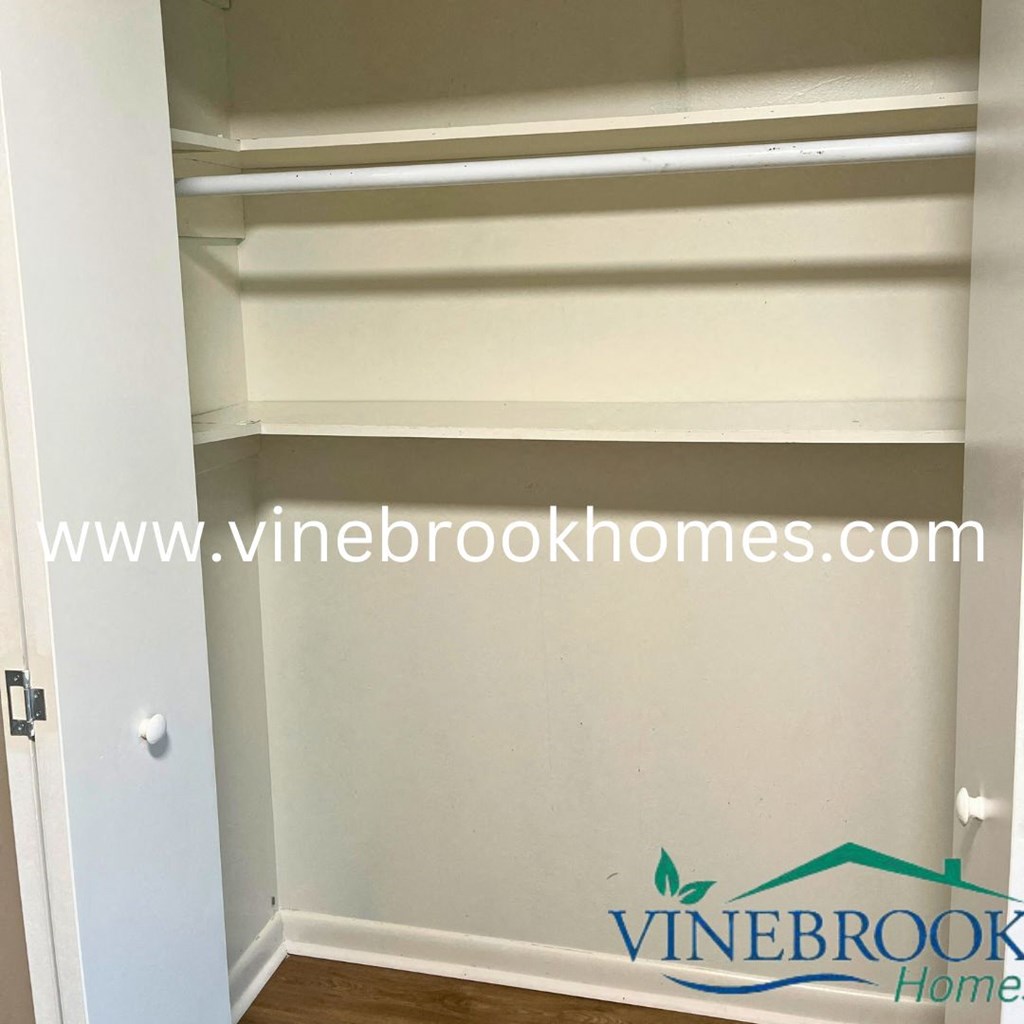 a closet with white shelves and a door with a vine brook homes logo