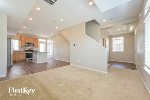 A spacious living room with a kitchen in the background and a carpet on the floor.