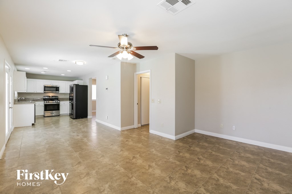 an empty living room with a ceiling fan and a kitchen