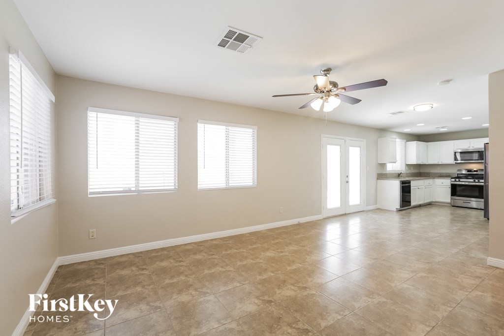 an empty living room with a ceiling fan and a kitchen
