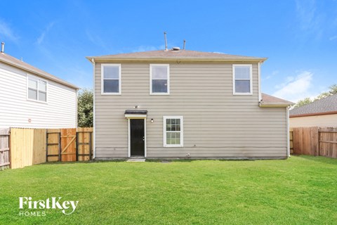 A house with a grey siding and a black door is shown with a grassy yard.