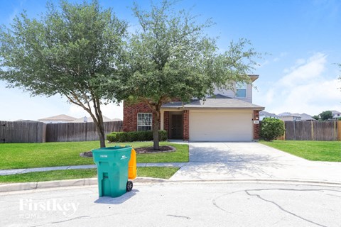 A green trash can is in front of a house.