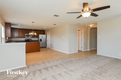 A spacious living room with a kitchen area in the background and a carpet on the floor.
