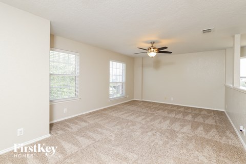 A spacious room with a carpeted floor and a ceiling fan.