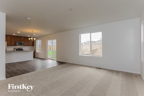 A spacious living room with a carpeted floor and a large window overlooking a barren landscape.