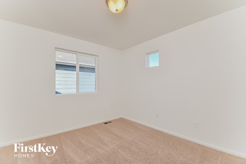 a bedroom with white walls and beige carpet and a window
