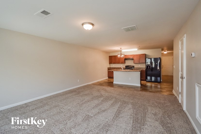an empty living room with a kitchen with a black refrigerator