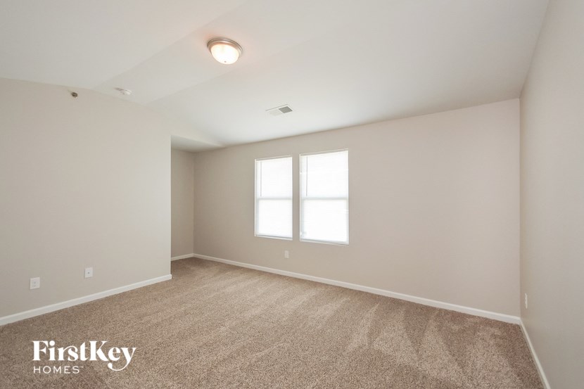 a spacious living room with carpet and two windows
