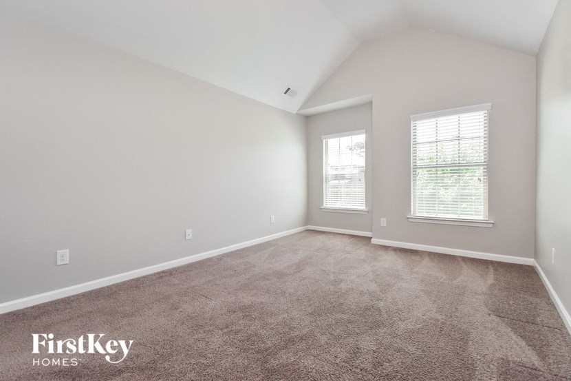 a spacious living room with carpet and two windows