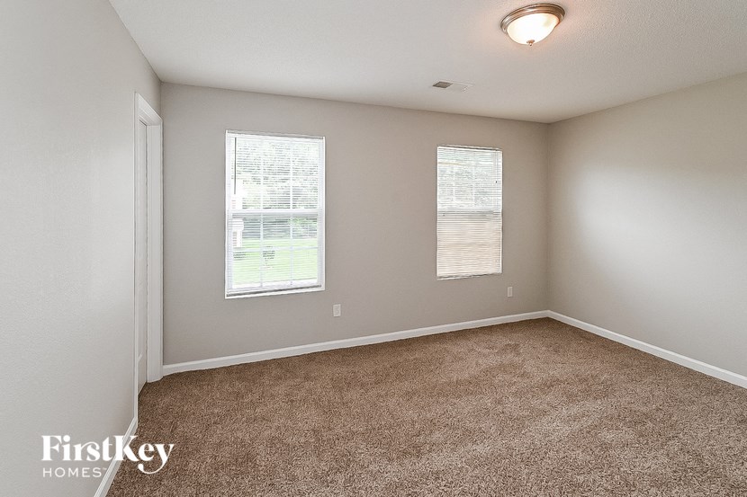 an empty bedroom with two windows and carpeting