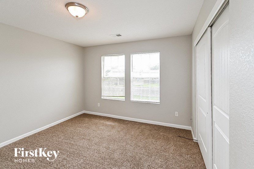 an empty bedroom with two windows and a closet