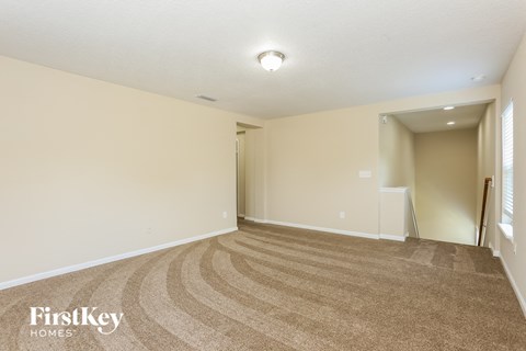 a spacious living room with carpet and a door to a hallway